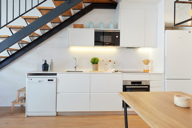 バルセロナにあるコンテンポラリースタイルのおしゃれなI型キッチン (アンダーカウンターシンク、フラットパネル扉のキャビネット、白いキャビネット、白いキッチンパネル、白い調理設備、無垢フローリング、アイランドなし、茶色い床、白いキッチンカウンター) の写真