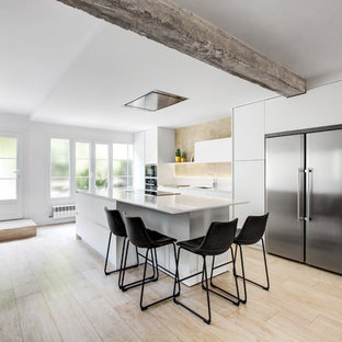 Diseño de cocina de galera, nórdica, abierta, con armarios con paneles lisos, puertas de armario blancas, electrodomésticos de acero inoxidable, una isla, encimeras blancas, fregadero bajoencimera, salpicadero beige, suelo de madera clara y suelo beige