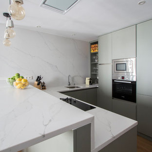 Diseño de cocina en L, actual, de tamaño medio, abierta, con fregadero bajoencimera, armarios con paneles lisos, puertas de armario verdes, encimera de mármol, salpicadero blanco, salpicadero de mármol, electrodomésticos de acero inoxidable, suelo de madera en tonos medios, península y suelo marrón