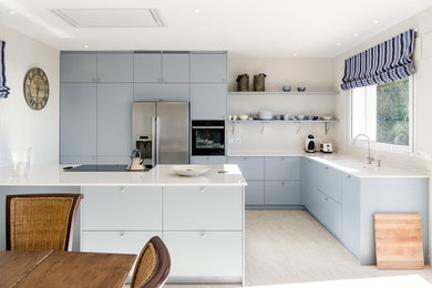 Bild på ett mellanstort minimalistiskt kök, med släta luckor, blå skåp, beige stänkskydd, rostfria vitvaror och en halv köksö