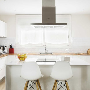 Foto de cocina en U, tradicional renovada, cerrada, con fregadero de un seno, encimera de madera, salpicadero blanco, salpicadero de azulejos tipo metro, electrodomésticos de acero inoxidable, suelo de madera clara, una isla, encimeras marrones, armarios con paneles empotrados, puertas de armario blancas y suelo beige