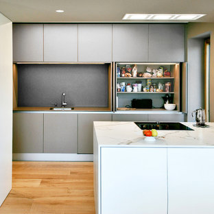 Imagen de cocina lineal, minimalista, de tamaño medio, abierta, con fregadero bajoencimera, armarios con paneles lisos, puertas de armario grises, encimera de cuarcita, salpicadero verde, electrodomésticos con paneles, suelo de madera en tonos medios, península y suelo marrón