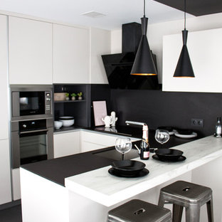Ejemplo de cocina en U, moderna, de tamaño medio, con armarios con paneles lisos, puertas de armario blancas, encimera de mármol, salpicadero negro, península, fregadero bajoencimera, electrodomésticos de acero inoxidable y suelo negro