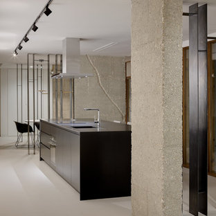 Imagen de cocina minimalista con armarios con paneles lisos, puertas de armario negras, una isla, encimeras negras, fregadero integrado, electrodomésticos negros, suelo de cemento y suelo gris