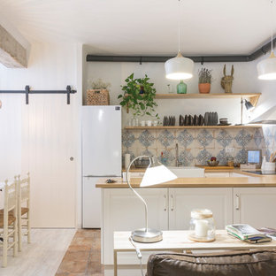 Imagen de cocina comedor en U, de estilo de casa de campo, con fregadero sobremueble, armarios con paneles con relieve, puertas de armario blancas, encimera de madera, salpicadero azul, electrodomésticos blancos, suelo de baldosas de terracota, península y suelo marrón