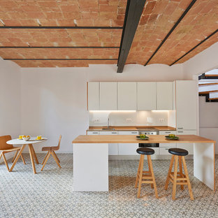 Foto de cocina de galera, mediterránea, con fregadero bajoencimera, armarios con paneles lisos, puertas de armario blancas, encimera de madera, electrodomésticos de acero inoxidable, una isla, suelo gris y encimeras marrones