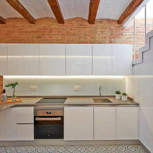Diseño de cocina mediterránea con fregadero bajoencimera, armarios con paneles lisos, puertas de armario blancas, salpicadero blanco, salpicadero de vidrio templado, península y encimeras grises