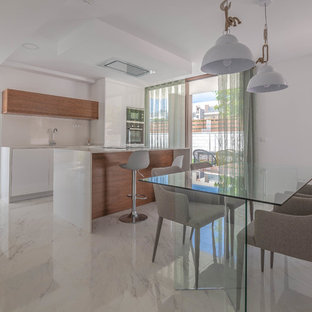 Modelo de cocina minimalista con puertas de armario de madera oscura, salpicadero blanco, electrodomésticos de acero inoxidable, suelo blanco y encimeras blancas