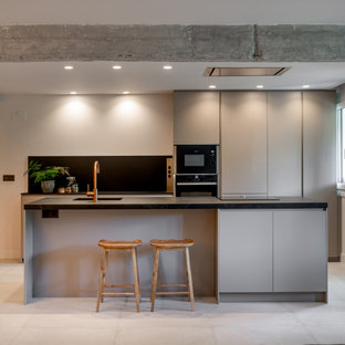 Foto de cocina de galera, moderna, con fregadero bajoencimera, armarios con paneles lisos, puertas de armario grises, electrodomésticos de acero inoxidable, una isla, suelo gris y encimeras negras
