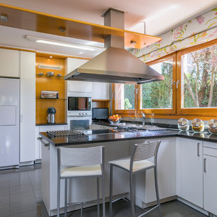 Diseño de cocina en U, contemporánea, con armarios con paneles lisos, puertas de armario blancas, electrodomésticos blancos, península, suelo gris y encimeras negras