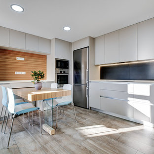 Diseño de cocina comedor en L, moderna, sin isla, con armarios con paneles lisos, salpicadero negro y electrodomésticos de acero inoxidable