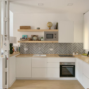 Ejemplo de cocina en L, actual, con fregadero encastrado, armarios con paneles lisos, puertas de armario blancas, encimera de madera, salpicadero verde, electrodomésticos de acero inoxidable, suelo de madera clara, suelo beige y encimeras beige