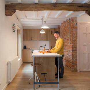 Diseño de cocina rural con armarios con paneles lisos, puertas de armario de madera clara, salpicadero blanco, suelo de madera clara, una isla, suelo beige y encimeras blancas