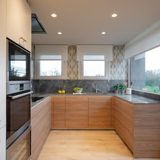 Diseño de cocina comedor en L, actual, grande, sin isla, con fregadero bajoencimera, armarios con paneles lisos, puertas de armario blancas, encimera de cuarzo compacto, salpicadero verde, puertas de cuarzo sintético, electrodomésticos de acero inoxidable, suelo laminado, suelo marrón y encimeras grises