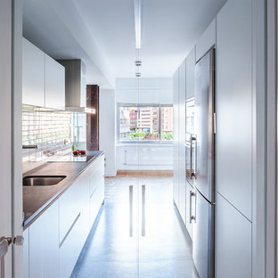 Diseño de cocina de galera, actual, grande, sin isla, con encimera de cuarzo compacto, suelo de cemento, suelo gris, armarios con paneles lisos, puertas de armario blancas, fregadero bajoencimera, salpicadero blanco, salpicadero de azulejos tipo metro y electrodomésticos de acero inoxidable