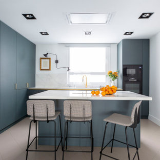 Ejemplo de cocina en L, contemporánea, de tamaño medio, cerrada, con armarios con paneles lisos, puertas de armario azules, salpicadero blanco, electrodomésticos con paneles, suelo de baldosas de porcelana, una isla, suelo gris y encimeras blancas
