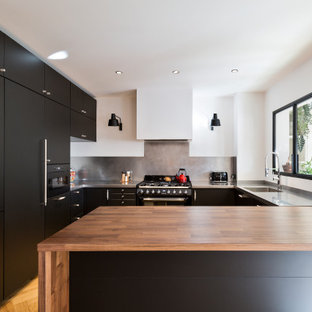 Foto de cocina en U, contemporánea, de tamaño medio, con fregadero integrado, armarios con paneles lisos, puertas de armario negras, encimera de acero inoxidable, salpicadero verde, electrodomésticos con paneles, península, suelo marrón y encimeras grises