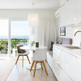 Ejemplo de cocina lineal, costera, de tamaño medio, abierta, sin isla, con armarios con paneles lisos, puertas de armario blancas, salpicadero blanco, electrodomésticos blancos, suelo de baldosas de cerámica, suelo beige, encimeras blancas y fregadero encastrado