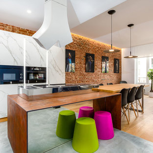 This is an example of an eclectic single-wall open plan kitchen in Madrid with black appliances, with island, flat-panel cabinets, marble floors, grey floor and orange benchtop.