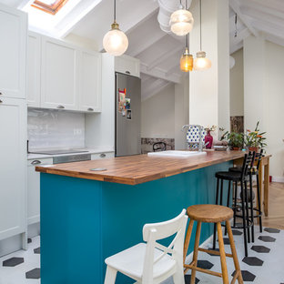 Ejemplo de cocina lineal, mediterránea, abierta, con armarios estilo shaker, una isla, salpicadero blanco, electrodomésticos de acero inoxidable, fregadero encastrado, puertas de armario turquesas, encimera de madera, suelo multicolor y encimeras marrones