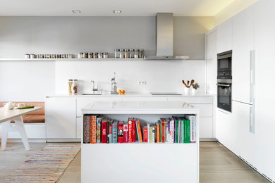 Einzeilige, Mittelgroße Moderne Wohnküche mit flächenbündigen Schrankfronten, weißen Schränken, Küchenrückwand in Weiß, Küchengeräten aus Edelstahl, hellem Holzboden, Kücheninsel und Unterbauwaschbecken in Madrid
