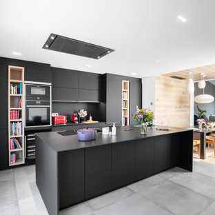 Foto de cocina de galera, contemporánea, grande, abierta, con armarios con paneles lisos, puertas de armario negras, salpicadero negro, una isla, suelo gris, encimeras negras, fregadero bajoencimera y electrodomésticos negros