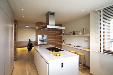 Ispirazione per una cucina minimal di medie dimensioni con ante lisce, ante in legno bruno, paraspruzzi bianco, parquet chiaro, penisola e pavimento beige