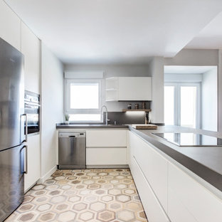 Modelo de cocina en U, nórdica, con electrodomésticos de acero inoxidable, encimeras grises, armarios con paneles lisos, puertas de armario blancas, encimera de cemento, salpicadero verde, suelo de azulejos de cemento, península y suelo beige