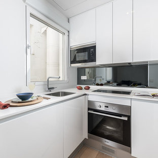 Diseño de cocina en L, nórdica, pequeña, abierta, sin isla, con fregadero bajoencimera, armarios con paneles lisos, puertas de armario blancas, encimera de cuarzo compacto, salpicadero verde, salpicadero de vidrio, electrodomésticos de acero inoxidable, suelo de madera clara, suelo beige y encimeras blancas