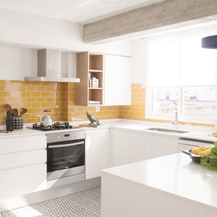 Imagen de cocina en U, actual, con fregadero bajoencimera, armarios con paneles lisos, puertas de armario blancas, salpicadero amarillo, salpicadero de azulejos tipo metro, electrodomésticos de acero inoxidable, península, suelo multicolor y encimeras blancas