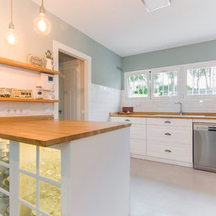 Foto de cocina en U, tradicional renovada, con puertas de armario blancas, encimera de madera, electrodomésticos de acero inoxidable, península, fregadero encastrado, armarios tipo vitrina, salpicadero blanco, salpicadero de azulejos tipo metro, suelo blanco y encimeras beige