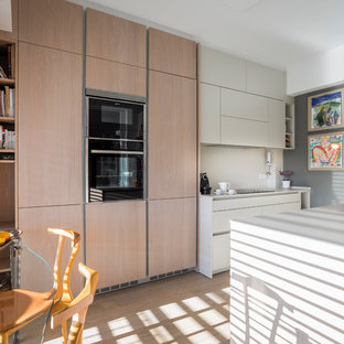 Diseño de cocina de galera, contemporánea, de tamaño medio, cerrada, sin isla, con armarios con paneles lisos, puertas de armario de madera clara, electrodomésticos negros, suelo de madera clara, suelo beige y encimeras blancas