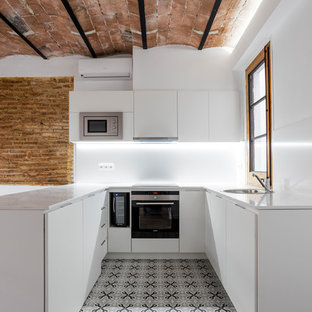 Modelo de cocina en U, mediterránea, pequeña, con armarios con paneles lisos, puertas de armario blancas, salpicadero blanco, electrodomésticos de acero inoxidable, suelo de baldosas de cerámica, península, fregadero encastrado, suelo gris y encimeras blancas