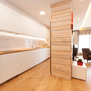 Modelo de cocina lineal, contemporánea, de tamaño medio, abierta, sin isla, con fregadero de doble seno, armarios con paneles lisos, puertas de armario blancas, encimera de madera, salpicadero blanco, salpicadero de azulejos de cerámica, electrodomésticos negros, suelo de madera clara, suelo marrón y encimeras marrones