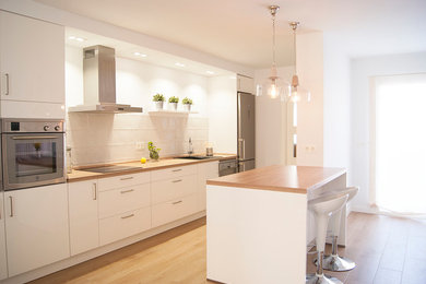 Photo of a medium sized contemporary single-wall kitchen/diner in Malaga with a submerged sink, flat-panel cabinets, white cabinets, wood worktops, white splashback, stainless steel appliances, light hardwood flooring and an island.