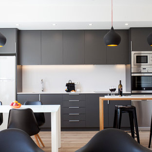 Diseño de cocina lineal, contemporánea, de tamaño medio, abierta, con armarios con paneles lisos, salpicadero blanco, electrodomésticos de acero inoxidable, suelo de madera en tonos medios, península, puertas de armario negras y suelo marrón