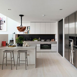 Foto di una grande cucina classica con ante lisce, ante bianche, elettrodomestici in acciaio inossidabile, parquet chiaro, paraspruzzi nero, penisola e top grigio