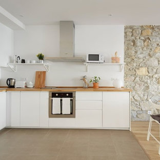 Ejemplo de cocina en L, mediterránea, abierta, sin isla, con fregadero encastrado, armarios con paneles lisos, puertas de armario blancas, encimera de madera, salpicadero blanco, suelo gris y encimeras beige
