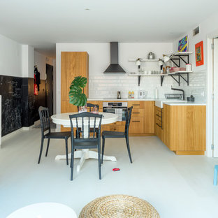 Diseño de cocina en L, nórdica, abierta, sin isla, con fregadero sobremueble, armarios con paneles lisos, puertas de armario de madera clara, salpicadero blanco, salpicadero de azulejos tipo metro, electrodomésticos negros, suelo gris y encimeras blancas