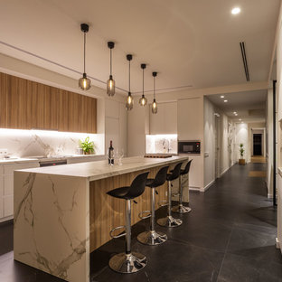 Imagen de cocina lineal, actual, con armarios con paneles lisos, puertas de armario de madera oscura, encimera de cuarzo compacto, salpicadero blanco, una isla, encimeras blancas y suelo negro