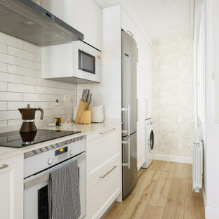 Foto de cocina de galera, clásica renovada, sin isla, con puertas de armario blancas, encimera de cuarzo compacto, salpicadero blanco, salpicadero de azulejos de cerámica, suelo laminado, encimeras blancas, armarios con paneles empotrados, electrodomésticos de acero inoxidable y suelo beige