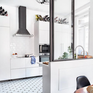 Imagen de cocina de galera, contemporánea, de tamaño medio, abierta, sin isla, con armarios con paneles lisos, puertas de armario blancas, salpicadero blanco, encimeras blancas, fregadero bajoencimera, encimera de cuarzo compacto, salpicadero de vidrio, electrodomésticos de acero inoxidable, suelo de baldosas de cerámica y suelo gris