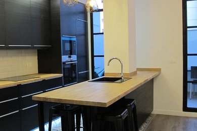 Foto de cocina comedor urbana con fregadero de un seno, puertas de armario negras, encimera de madera, suelo de madera clara, una isla y suelo gris