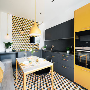 Foto de cocina comedor en L, actual, con armarios con paneles lisos, puertas de armario amarillas, salpicadero multicolor, electrodomésticos negros, suelo multicolor y encimeras grises