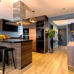 Imagen de cocina en L, contemporánea, de tamaño medio, con armarios con paneles lisos, puertas de armario de madera oscura, salpicadero verde, electrodomésticos negros, suelo de madera en tonos medios, una isla, suelo beige y encimeras negras