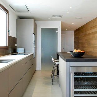 Modelo de cocina lineal, contemporánea, con fregadero de doble seno, armarios con paneles lisos, puertas de armario grises, salpicadero metalizado, una isla, suelo gris y encimeras negras