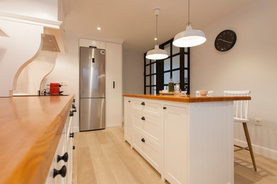 Ejemplo de cocina lineal nórdica de tamaño medio abierta con armarios con paneles empotrados, puertas de armario blancas, encimera de madera, salpicadero blanco, suelo de madera clara y una isla