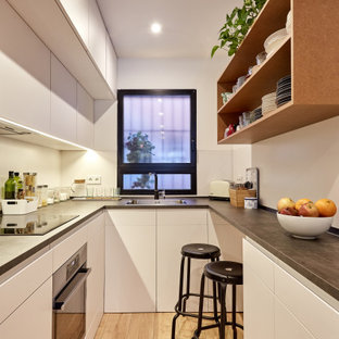 Diseño de cocina en U, actual, pequeña, cerrada, con fregadero encastrado, armarios con paneles lisos, puertas de armario blancas, salpicadero blanco, electrodomésticos de acero inoxidable, suelo de madera clara, suelo beige y encimeras grises