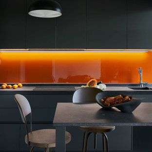 Imagen de cocina de galera, contemporánea, grande, con fregadero bajoencimera, armarios con paneles lisos, puertas de armario grises, salpicadero naranja, salpicadero de vidrio templado, electrodomésticos con paneles, una isla, suelo gris y encimeras grises