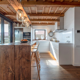Modelo de cocina en L, de estilo de casa de campo, con armarios con paneles lisos, puertas de armario blancas, electrodomésticos de acero inoxidable, suelo de madera en tonos medios, una isla, suelo marrón y encimeras blancas